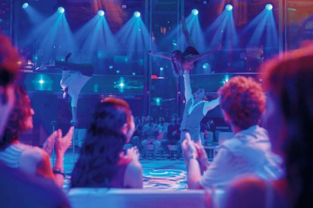 Dancers performing on illuminated stage with blue spotlight beams during evening entertainment show on cruise ship deck with 